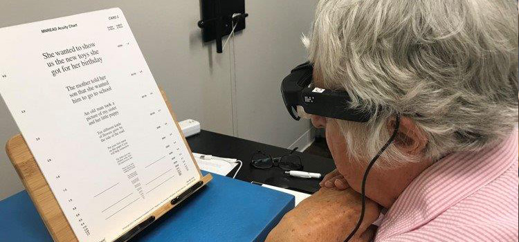 photo of an older person using a head-mounted assistive reading device to read the MNREAD Acuity Chart