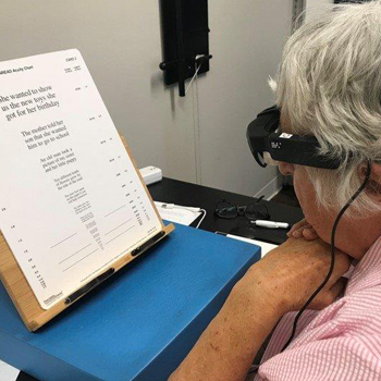 photo of an older person using a head-mounted assistive reading device to read the MNREAD Acuity Chart