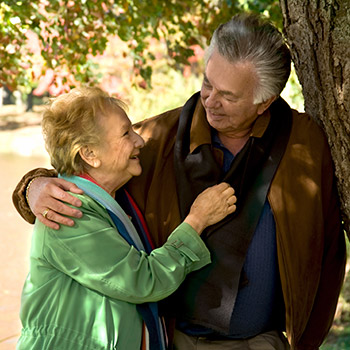 Elderly couple under tree smiling